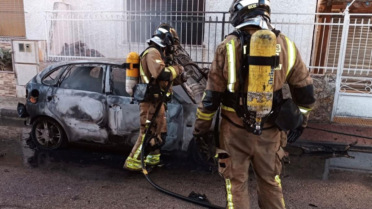 Dos bomberos sofocando las llamas del vehículo.