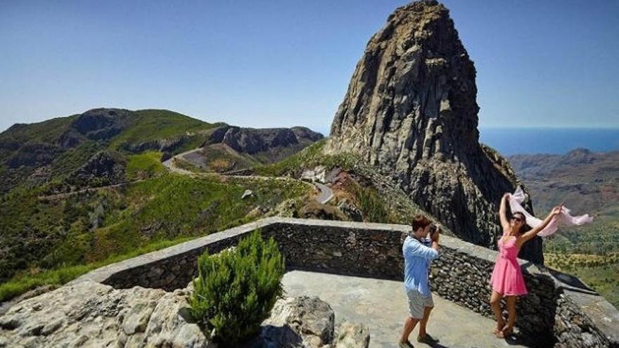 Unos turistas se fotografían con el Roque de Agando al fondo.