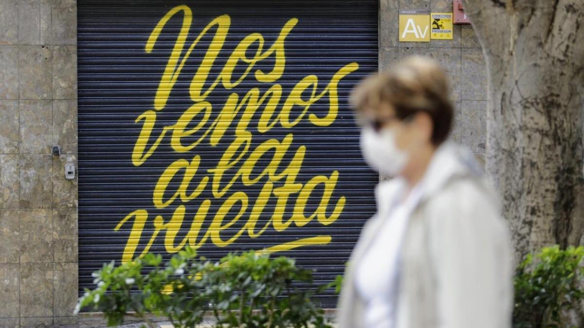 Una mujer con mascarilla pasea por delante de un comercio cerrado.