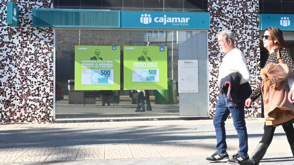 Un grupo de personas pasea delante de la sucursal de una entidad financiera de Castellón.