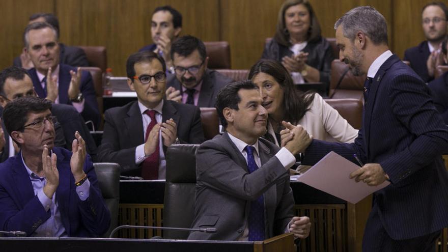 El presidente de la Junta de Andalucía, Juanma Moreno (c), saluda al Consejero de Hacienda, Juan Bravo (d), tras la intervención del consejero