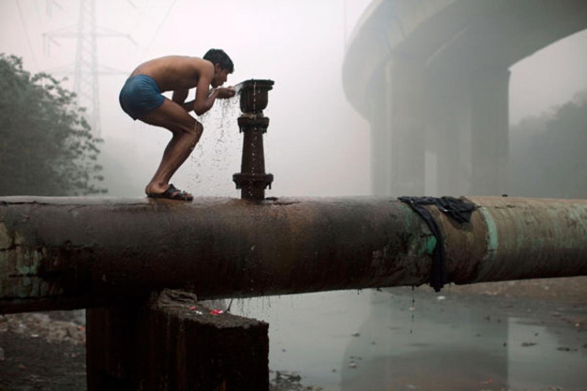 Un home beu d’una canonada en un fred matí cobert de boira, a Nova Delhi (Índia).