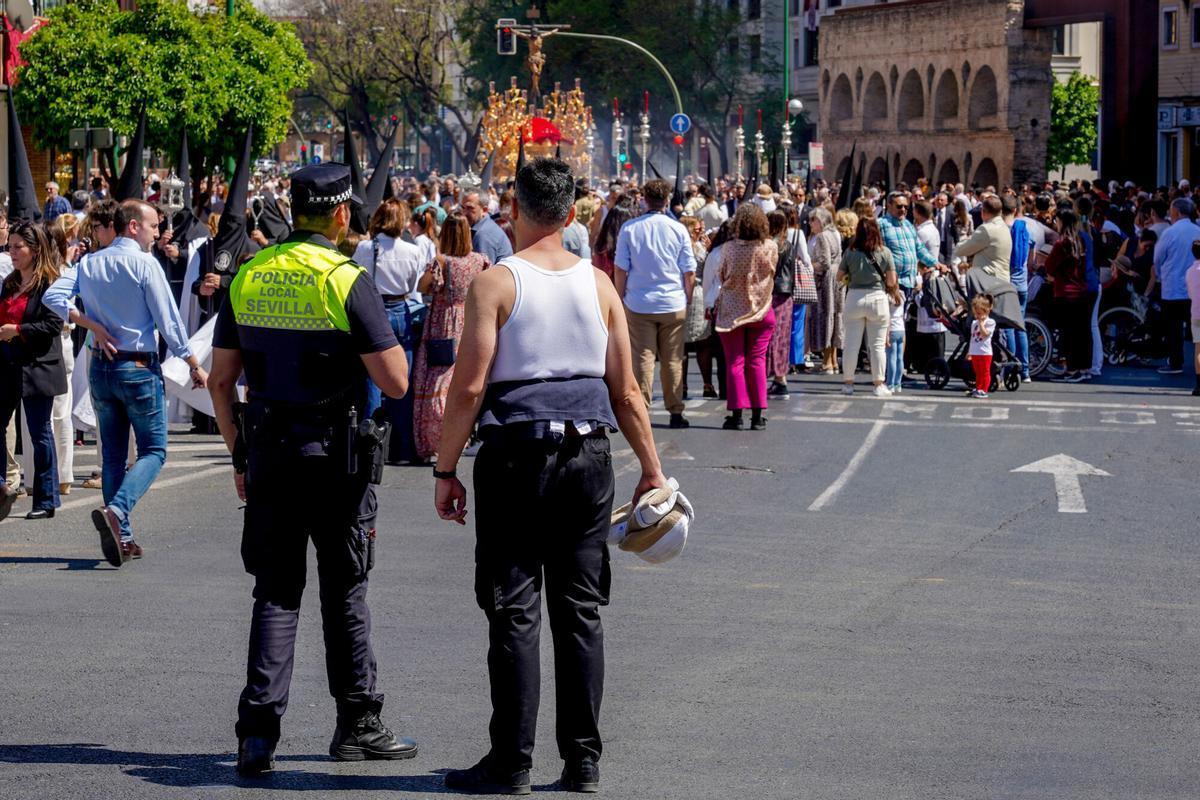 Un policía municipal y un costalero viendo el cortejo de la Hermandad de la Sed. El Ayuntamiento establece cortes de tráfico por la Semana Santa de Sevilla 2026.