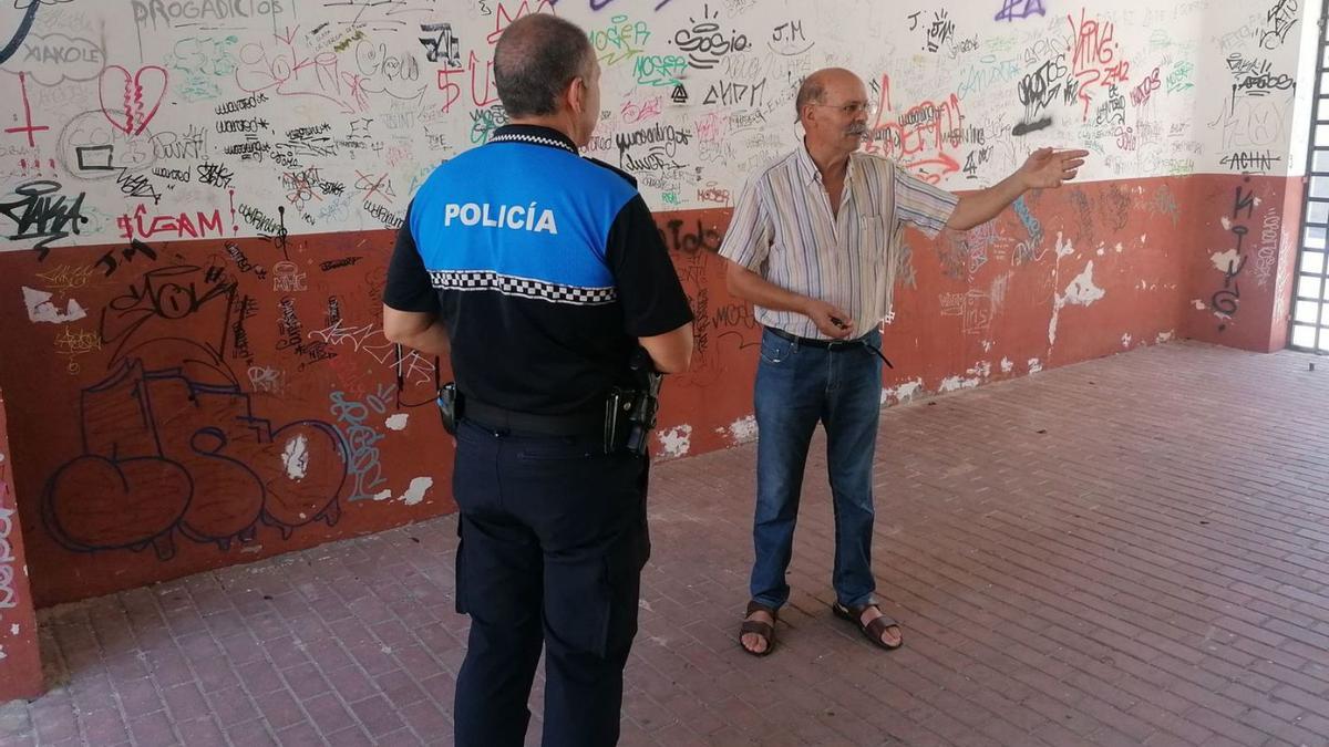 Martín Arroyo comenta con un policía local las pintadas del edificio de acceso al pabellón de deportes. | M. J. C.