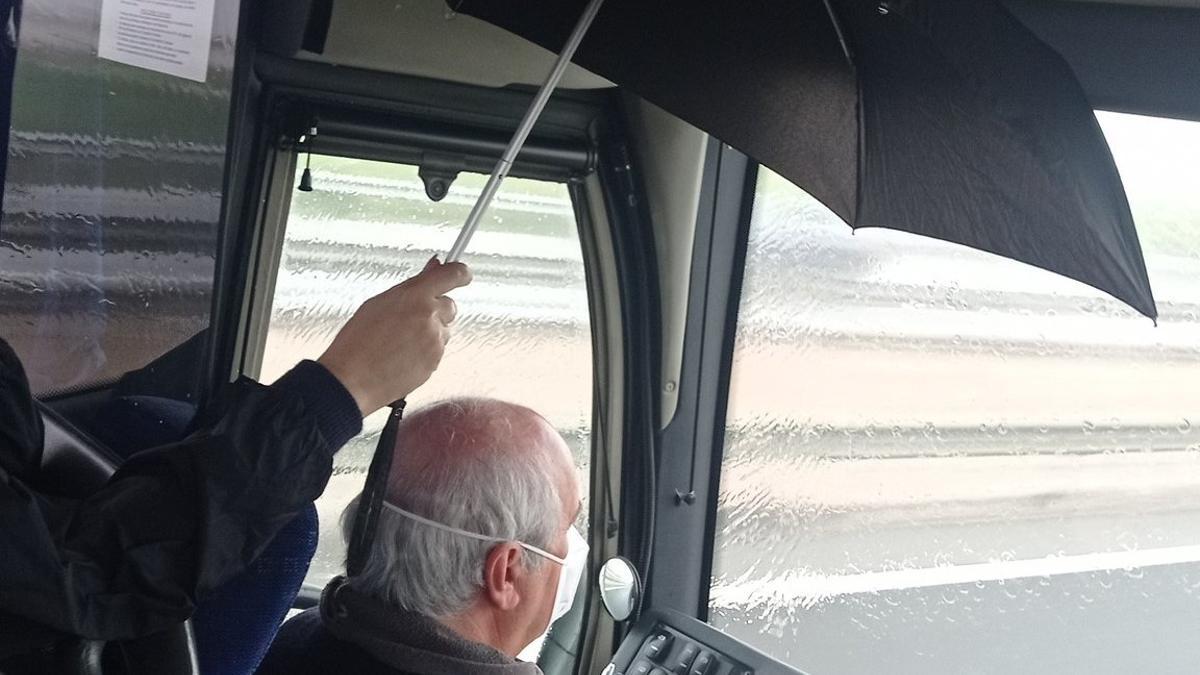 Un conductor de autobús viaja hacia Cartagena protegido por un paraguas ante las goteras del techo del vehículo.