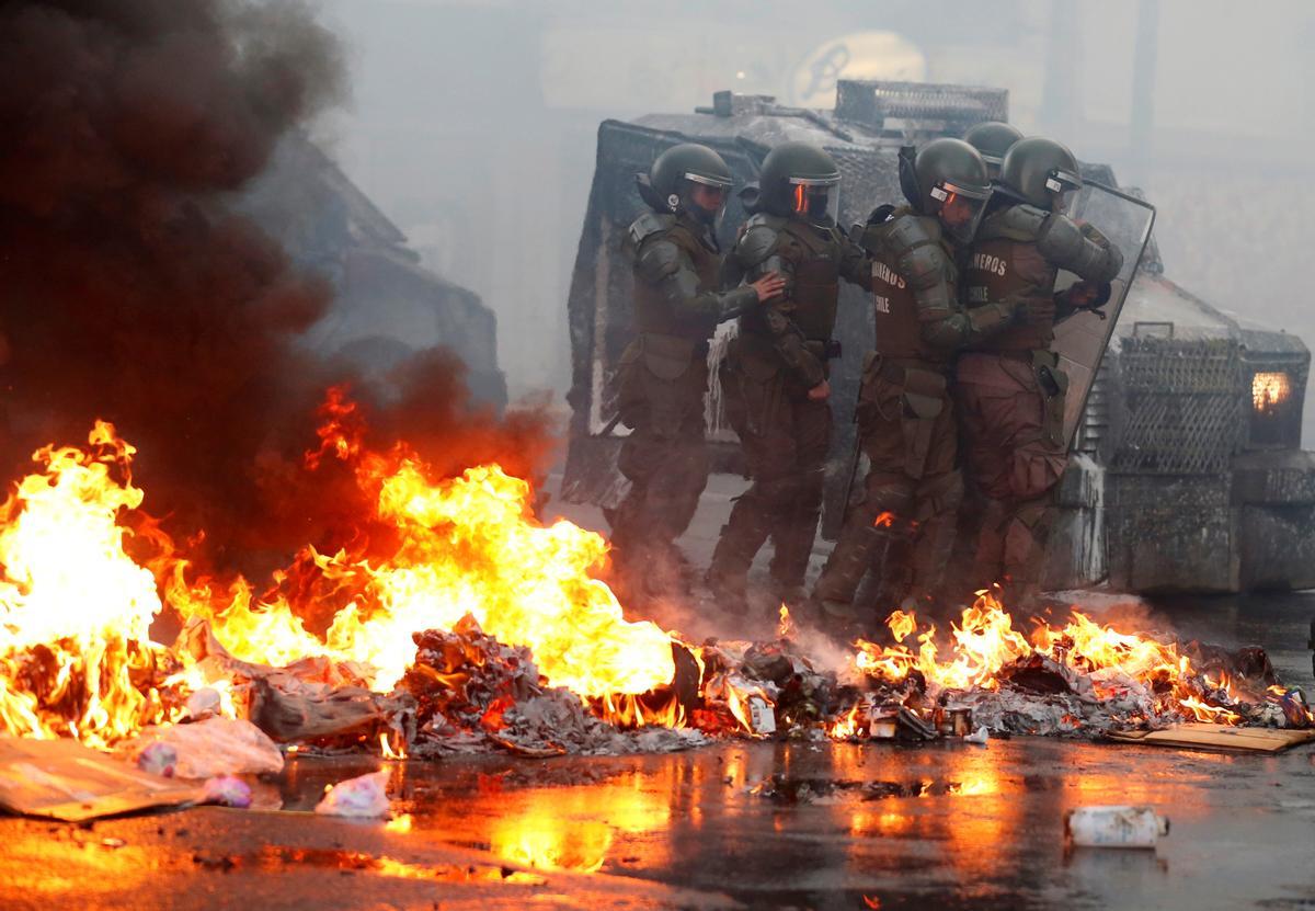 Un grupo de antidisturbios pasa frente a un vehículo en llamas durante una protesta en Valparaíso, en febrero de 2020.