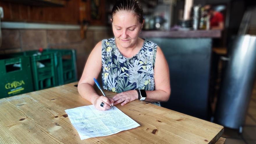 Verónica Fernández firma una de las hojas que están a disposición de los vecinos en las sidrerías y comercios de Requejo. | A. Velasco