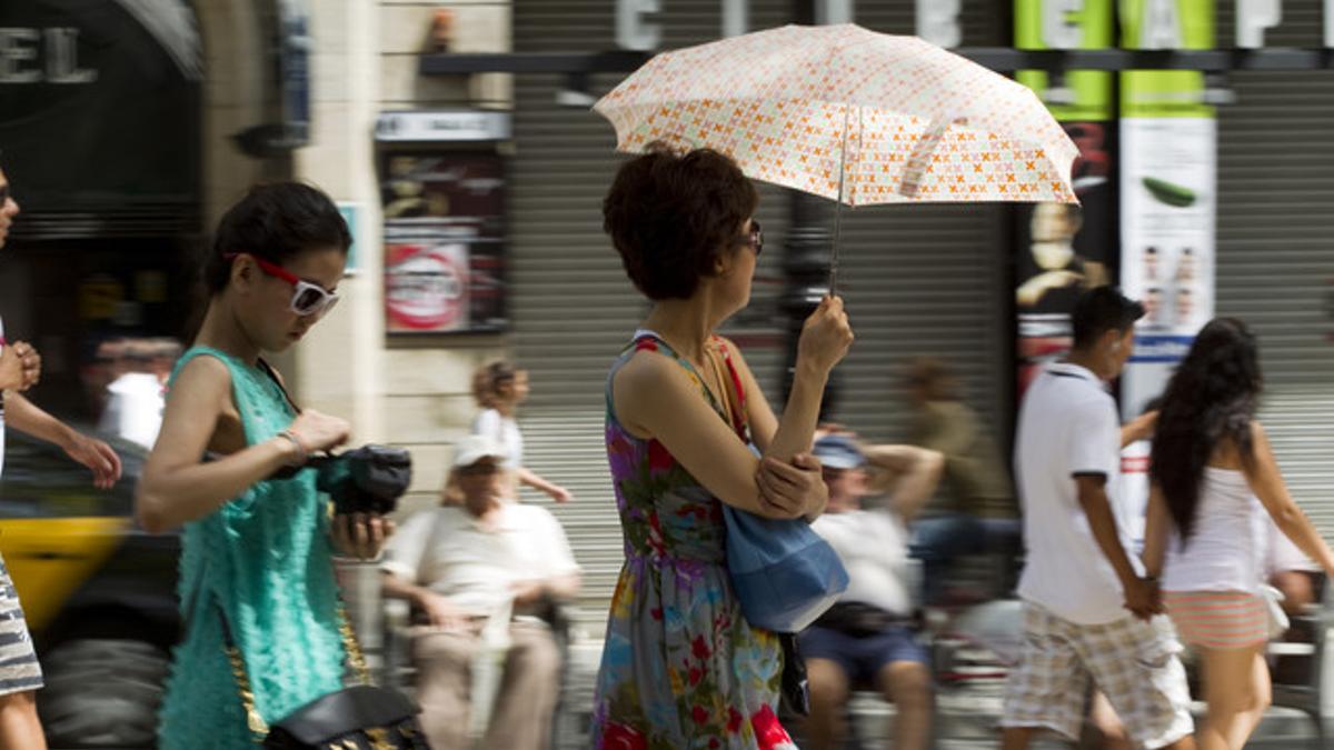 Unas turistas pasean por las Ramblas con paraguas.