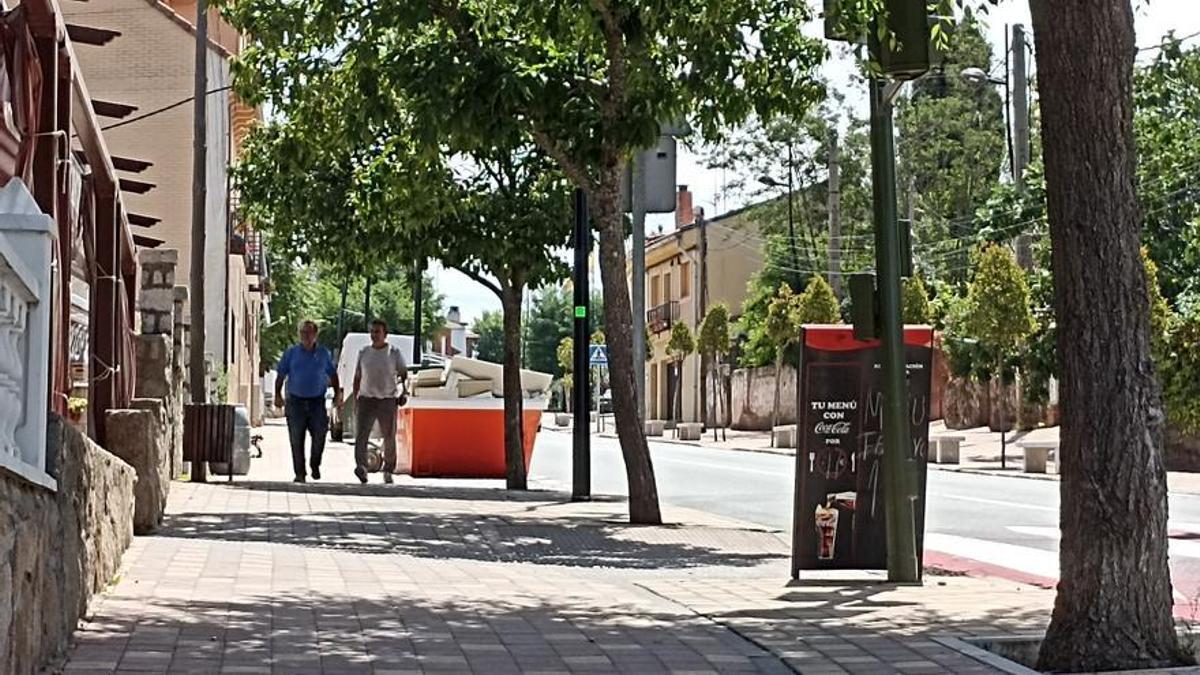 Dos personas pasean por la acera de la carretera principal que cruza Rozas de Puerto Real.