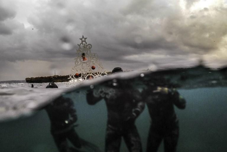 Buceadores posan con un árbol navideño ornamental en la superficie del agua, antes de bajar a colocarlo en el fondo del mar cerca de la costa de la ciudad portuaria de Tripoli, en Líbano. 18 de diciembre de 2018. IBRAHIM CHALHOUB / AFP