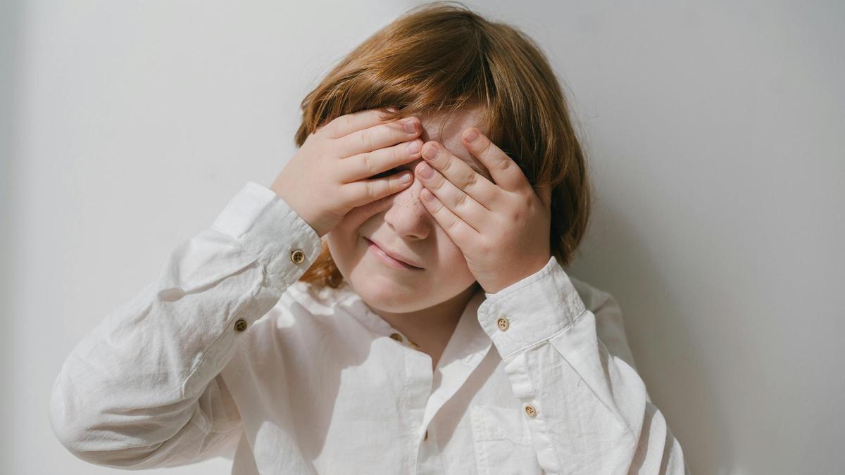 Un niño observa mientras realiza el gesto de taparse los ojos con las manos.