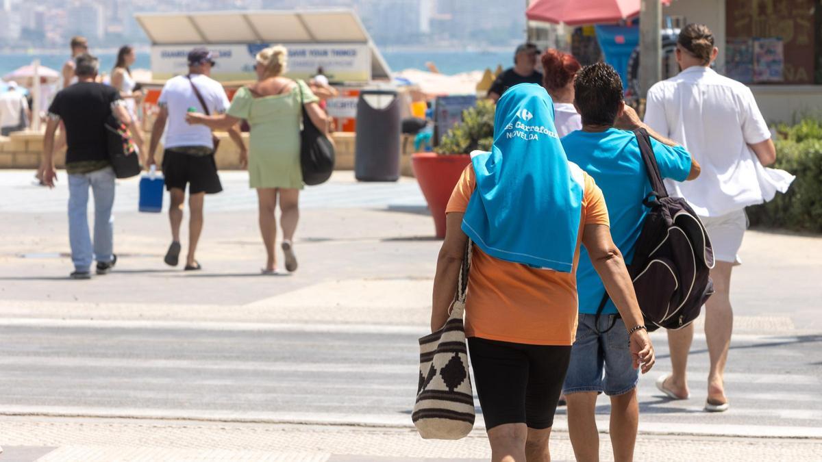 Una mujer se protege la cabeza del sol con una camiseta en la playa del Postiguet de Alicante en una imagen de este verano.