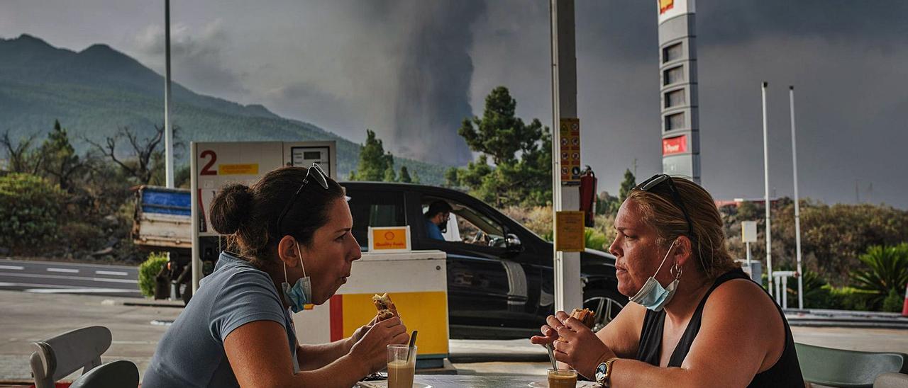 Dos mujeres desayunan en la gasolinera de El Paso. A pocos metros, el volcán emana una gran nube de gases.