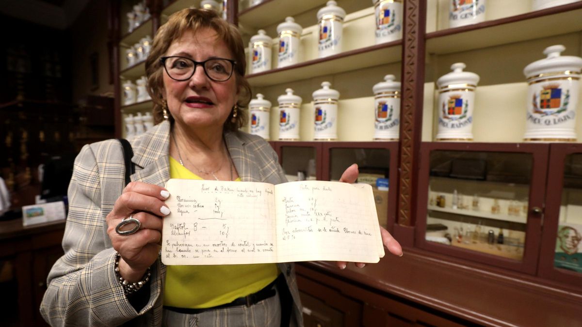 Un cuaderno con las instrucciones, a mano, para elaborar un medicamento, con los botes centenarios detrás.