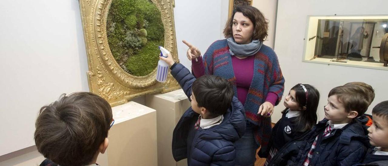 Arriba, un niño riega el musgo de una pieza durante una visita escolar. A la derecha, varias obras de la exposición. // Cristina Graña