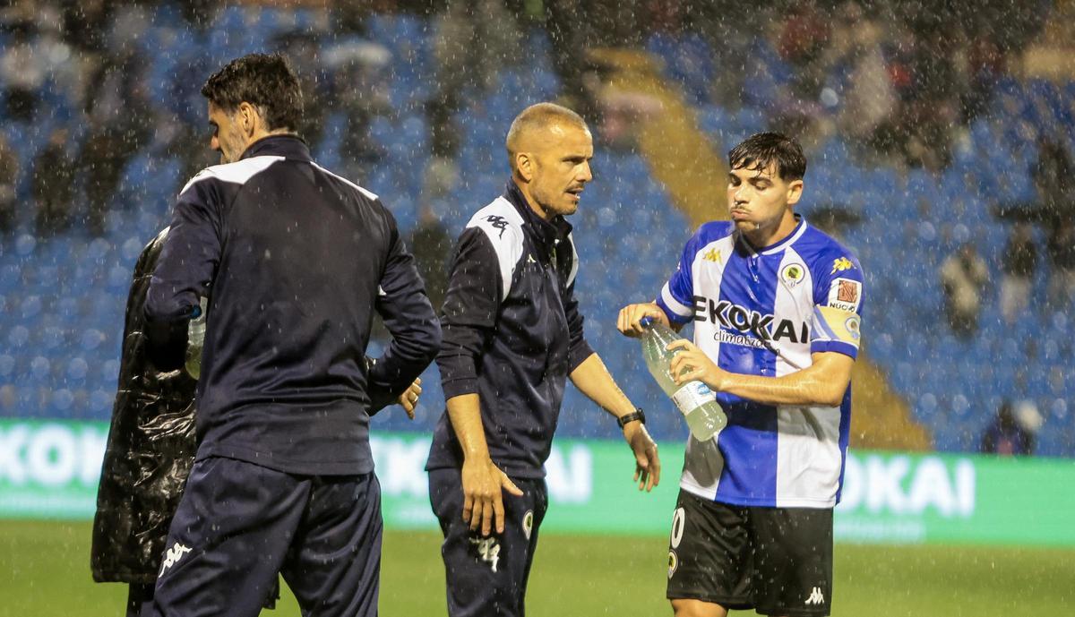 Beto Company observa el desarrollo del Hércules-Atlético Sanluqueño en pleno aguacero mientras el capitán Nico Espinosa se hidrata en la banda.