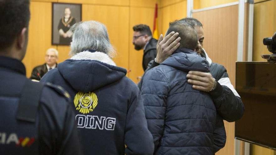 Los dos hermanos acusados se abrazan en el juicio, junto a su padre, de espaldas.