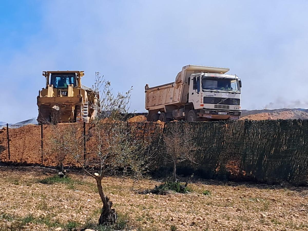 Una excavadora y un camión retirando arena para llevarla y depositarla sobre el incendio de la planta de reciclaje de Requena.