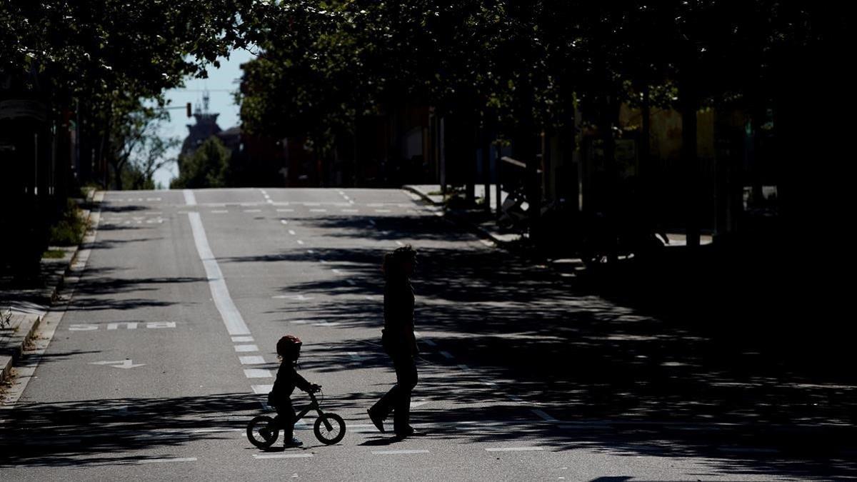 Un niño en bicicleta acompaña a una mujer en una calle de Barcelona.