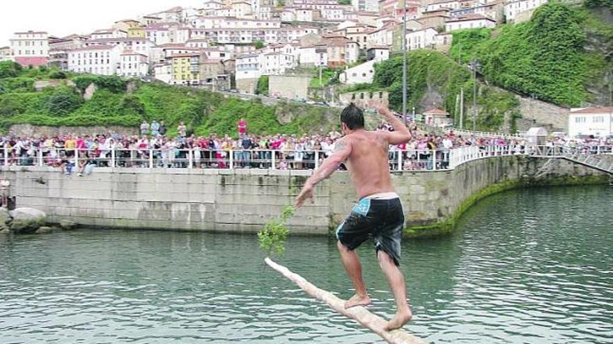 Uno de los participantes en el concurso de cucaña, con la villa de Lastres al fondo.