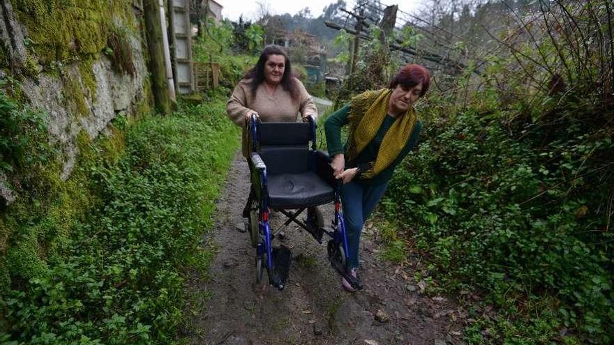 Dos vecinas de Vilar empujan una silla de ruedas para llegar a una ambulancia en la carretera. // G.Santos