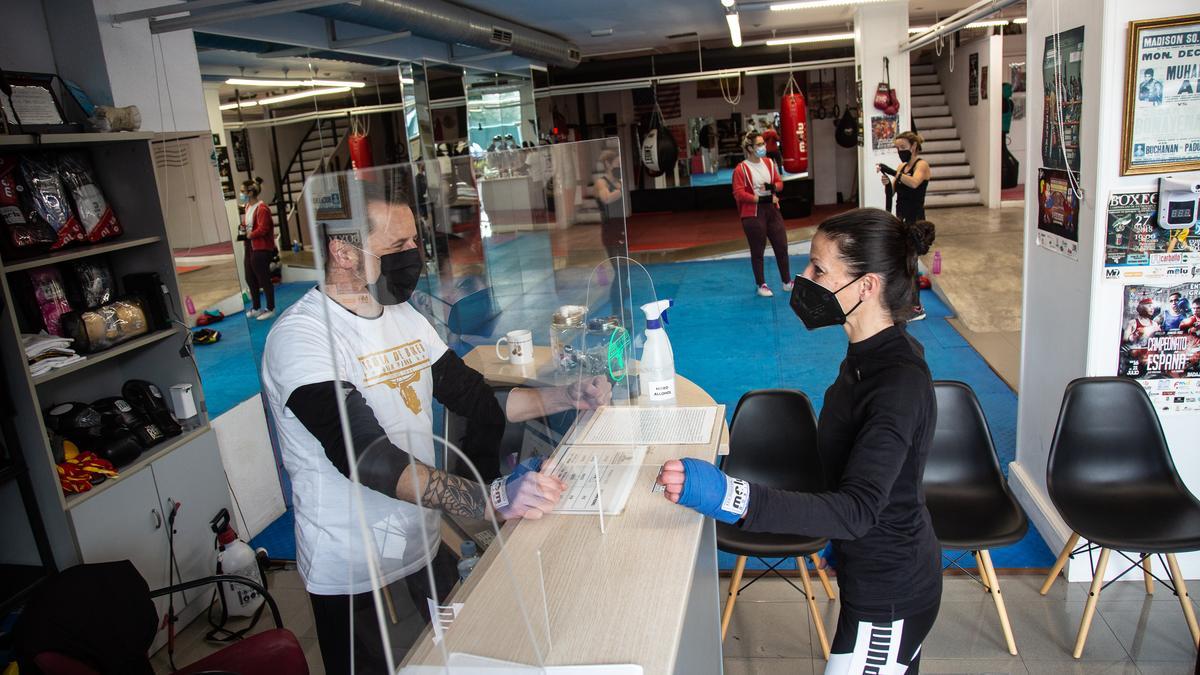 Una clienta con mascarilla es atendida en la recepción de una escuela de boxeo.