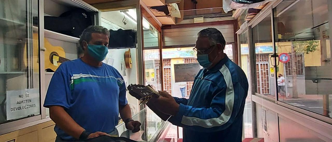 Antonio Falcón (a la izquierda), heredero de la tienda ‘Falcón’ de música y pesca, mostrando una de las guitarras en venta | | J.P.