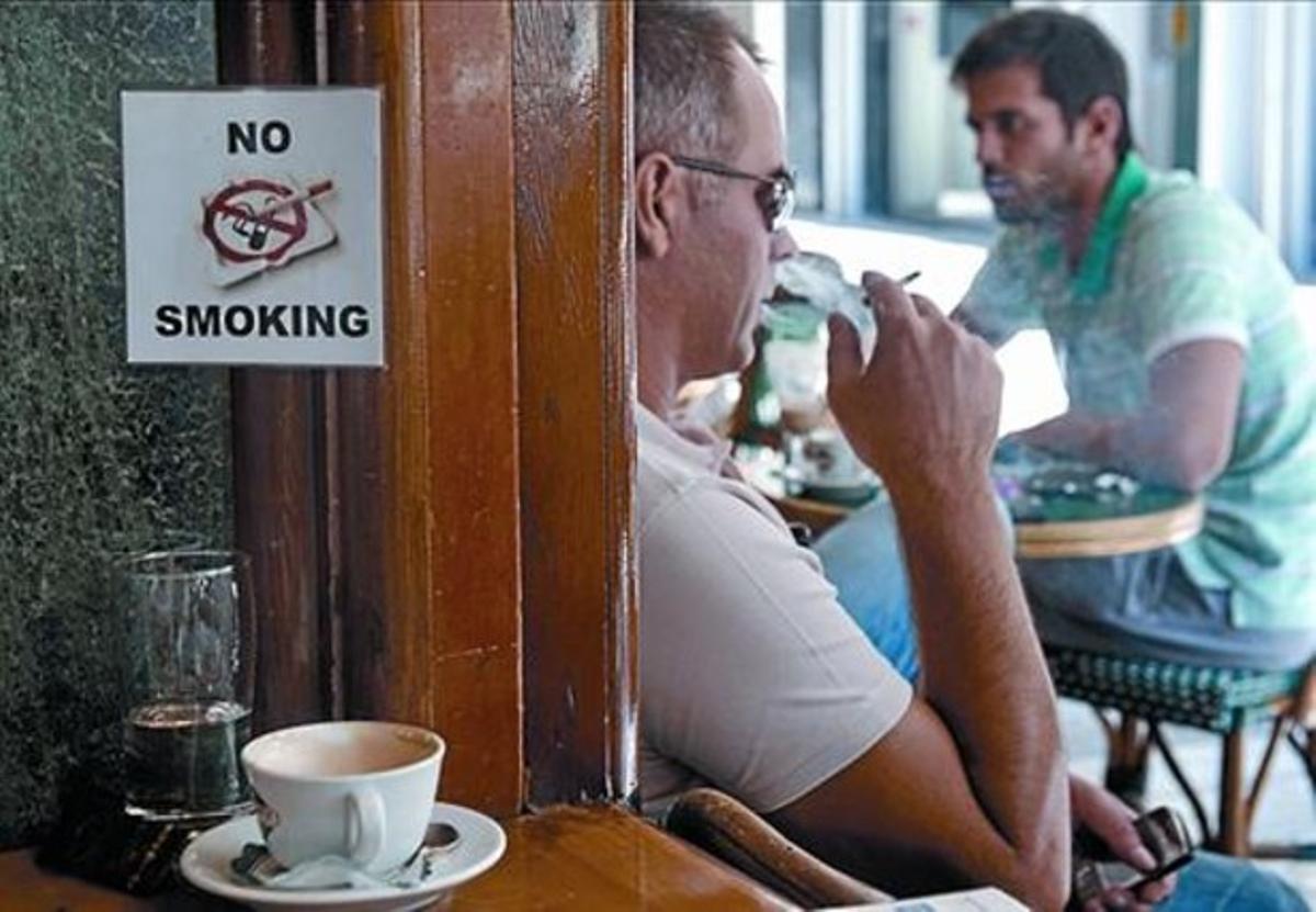 Un home fuma un cigarret a la terrassa d’un bar d’Atenes, ahir.