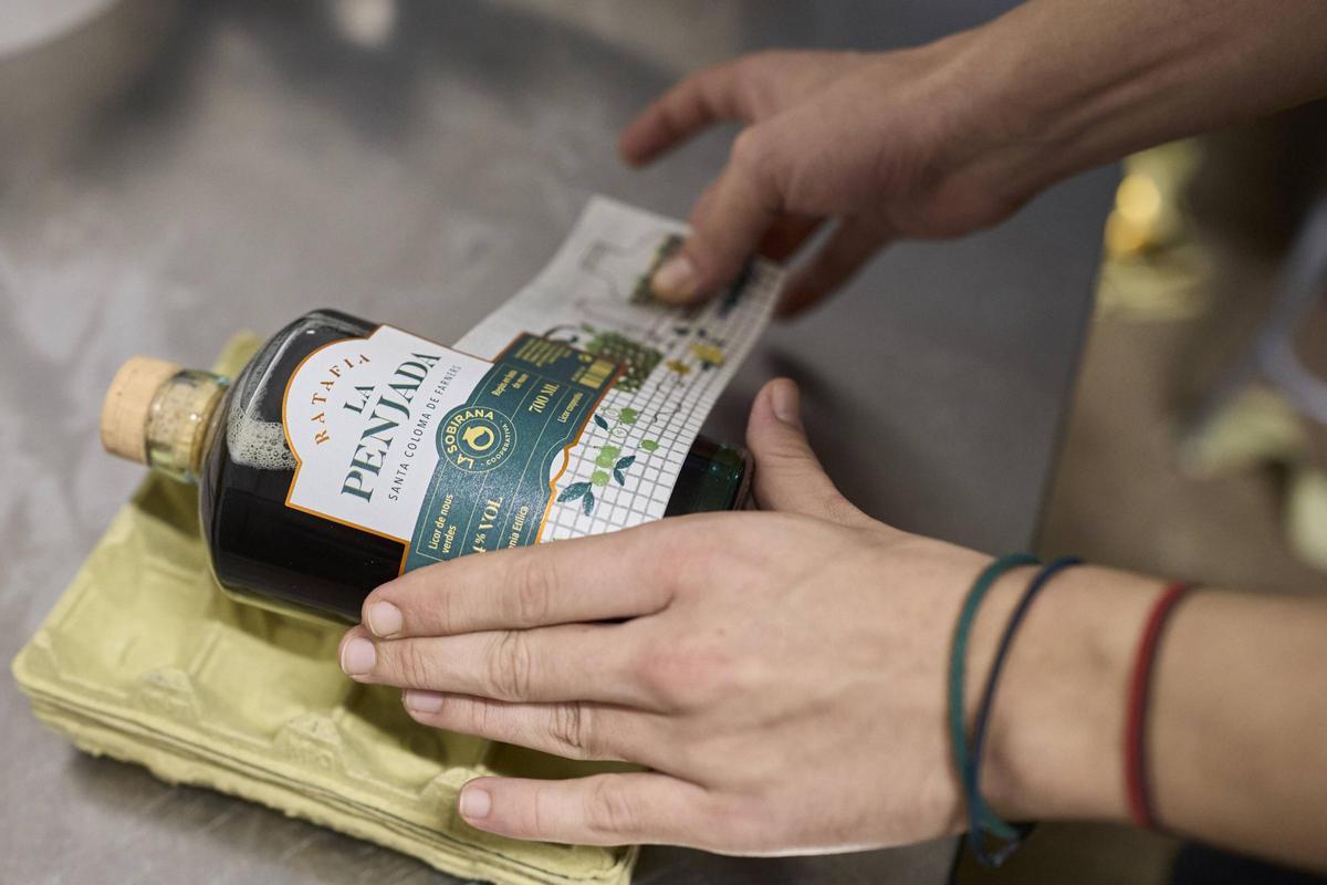 Un membre de la cooperativa etiquetant una ampolla de La Penjada, a l'obrador de La Sobirana.
