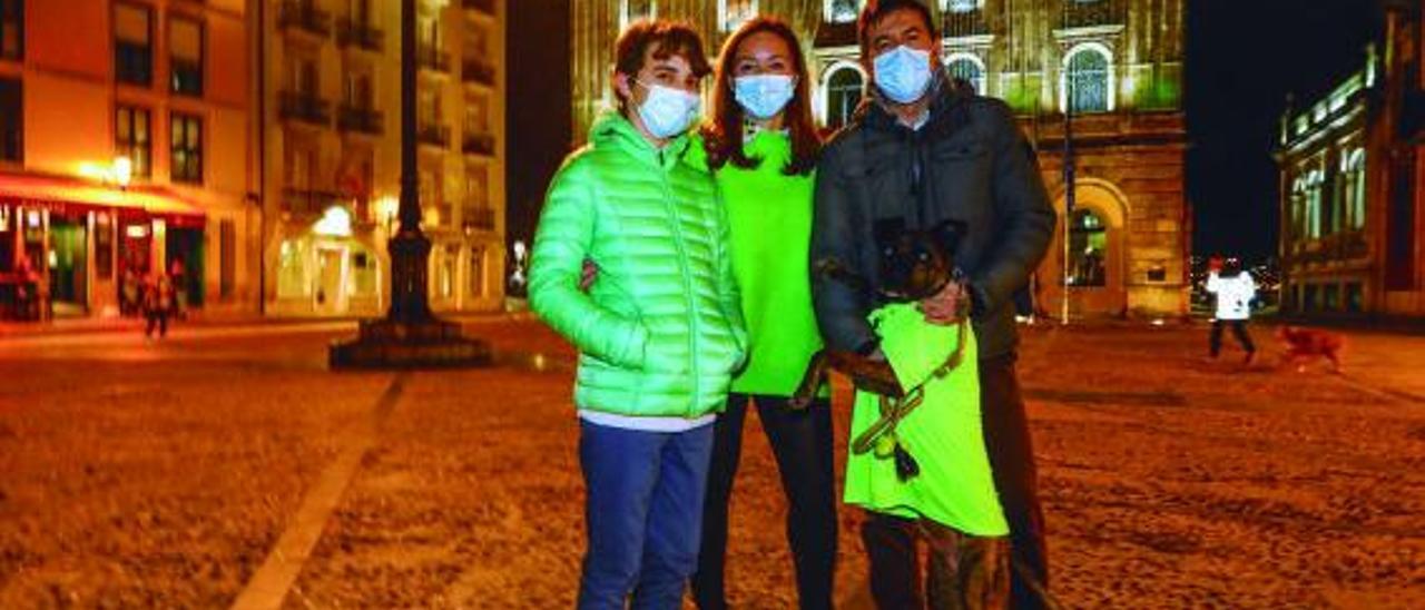 Ricardo Tucho, afectado por la  enfermedad de Perthes; su madre, Mónica Lombán; José Carlos  Reigosa y su perro, “Beto”,  ante el Ayuntamiento de Gijón,  iluminado de verde. | Marcos León