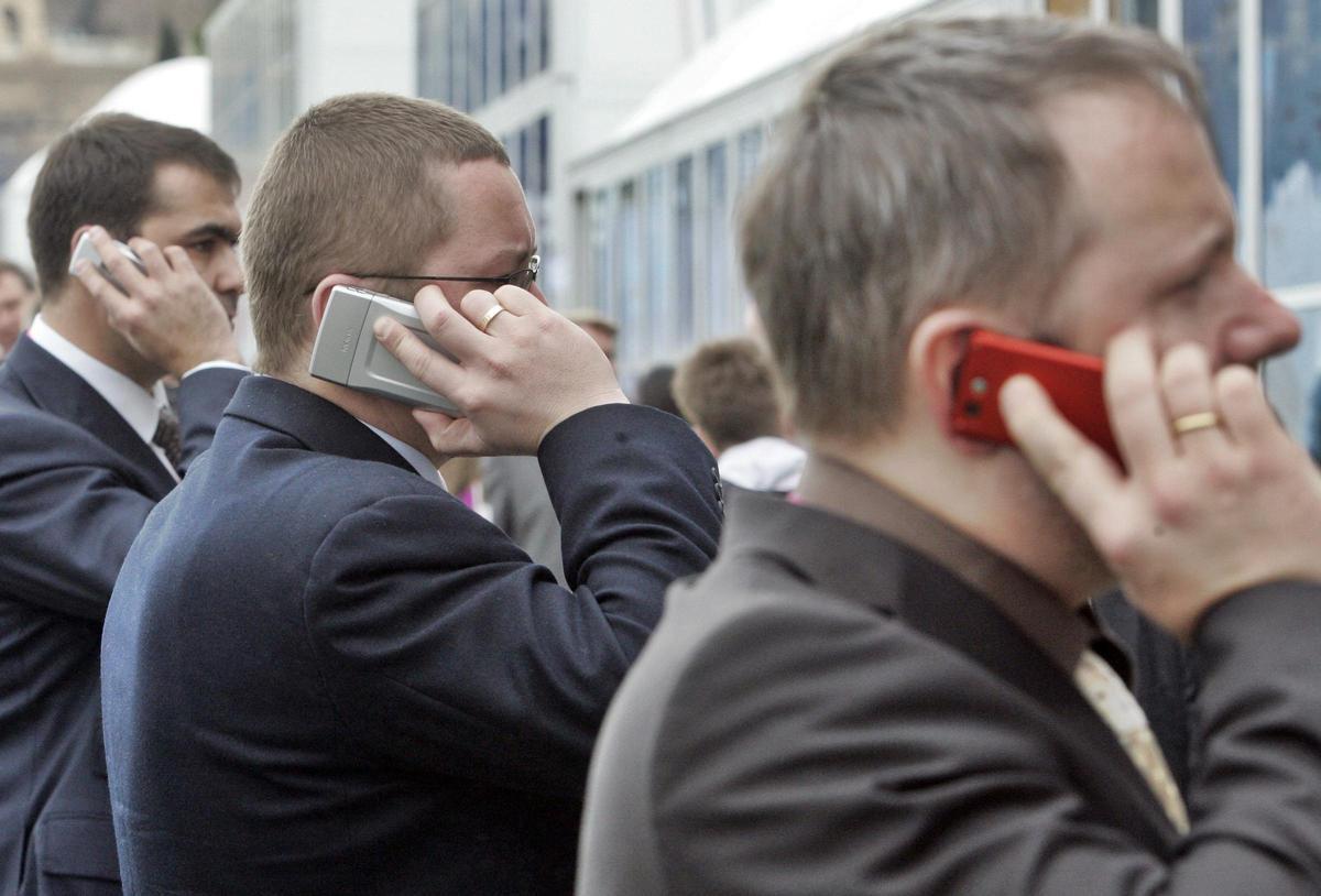 Tres hombres hablan por teléfono móvil en el congreso internacional 3GSM de Barcelona.