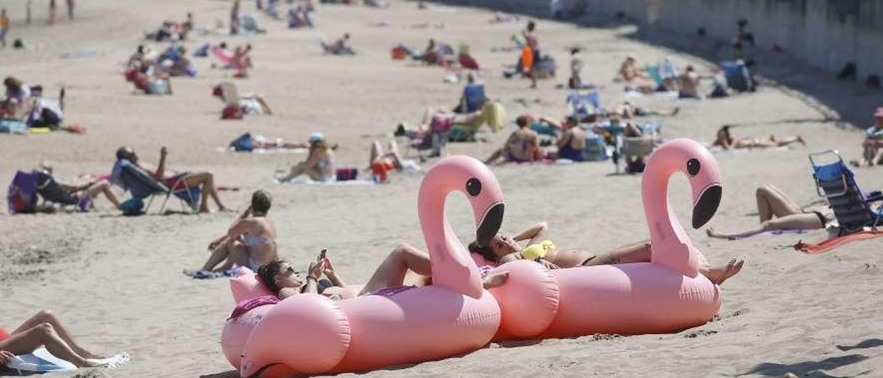 Dos flotadores de flamenco en la playa de Salinas. En el círculo, María Robles, con su unicornio en la playa castrillonense.