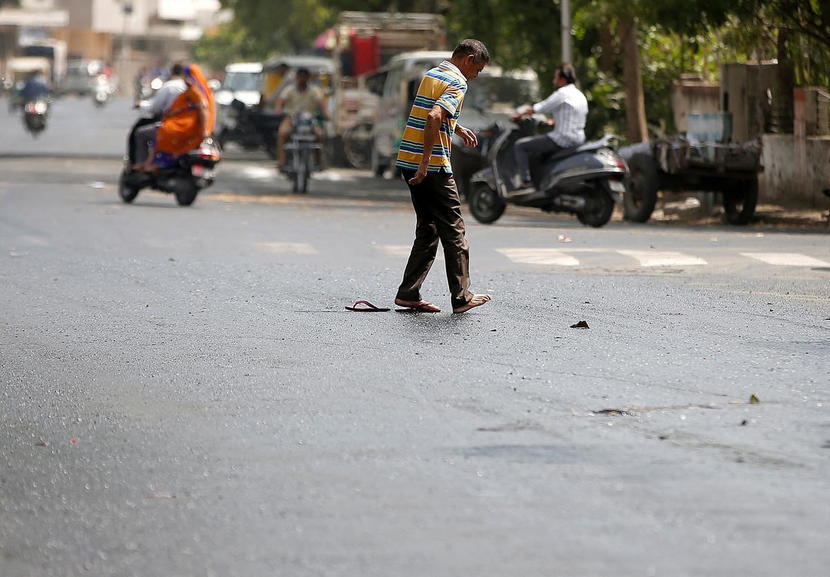 Un hombre intenta cruzar una calle después de que sus chanclas se atascaran en alquitrán derretido en un día caluroso en Ahmedabad, India.