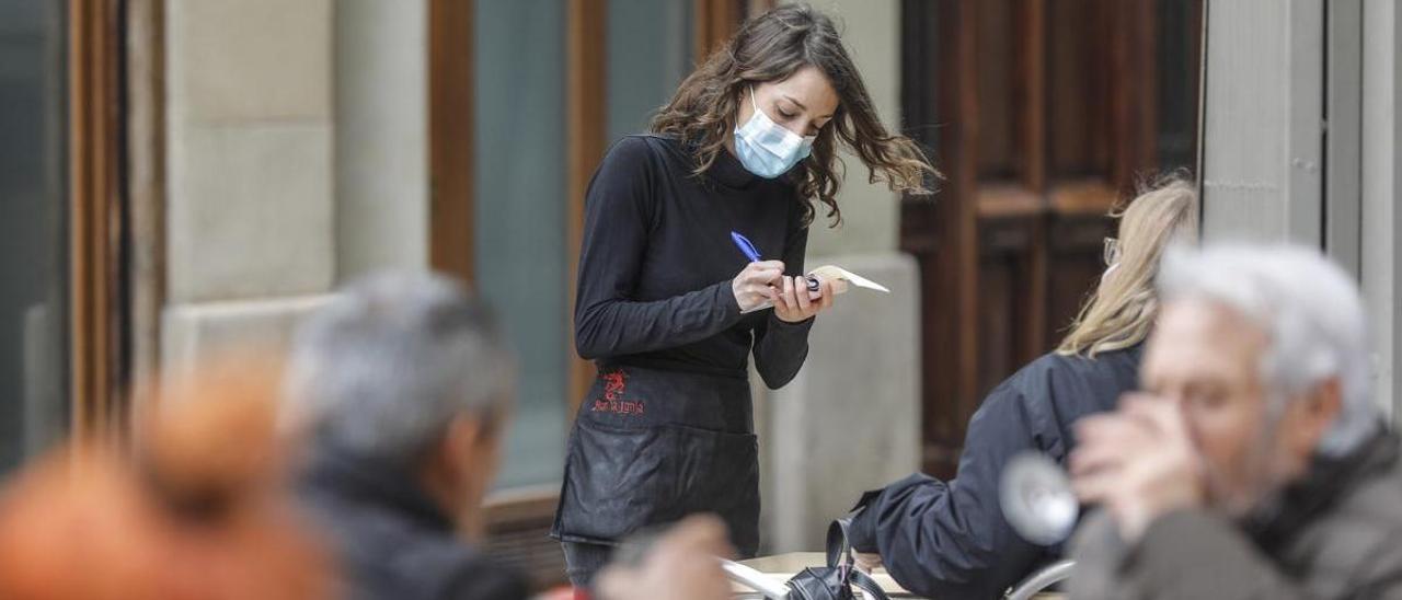 Una camarera atiende a varios clientes en una terraza.