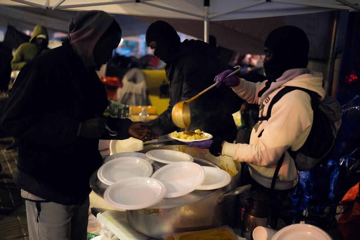 Voluntarios de distintas entidades privadas reparten comida para la cena de Nochebuena bajo la autopista C-31, donde aún duermen decenas de personas desalojadas del antiguo instituto B9