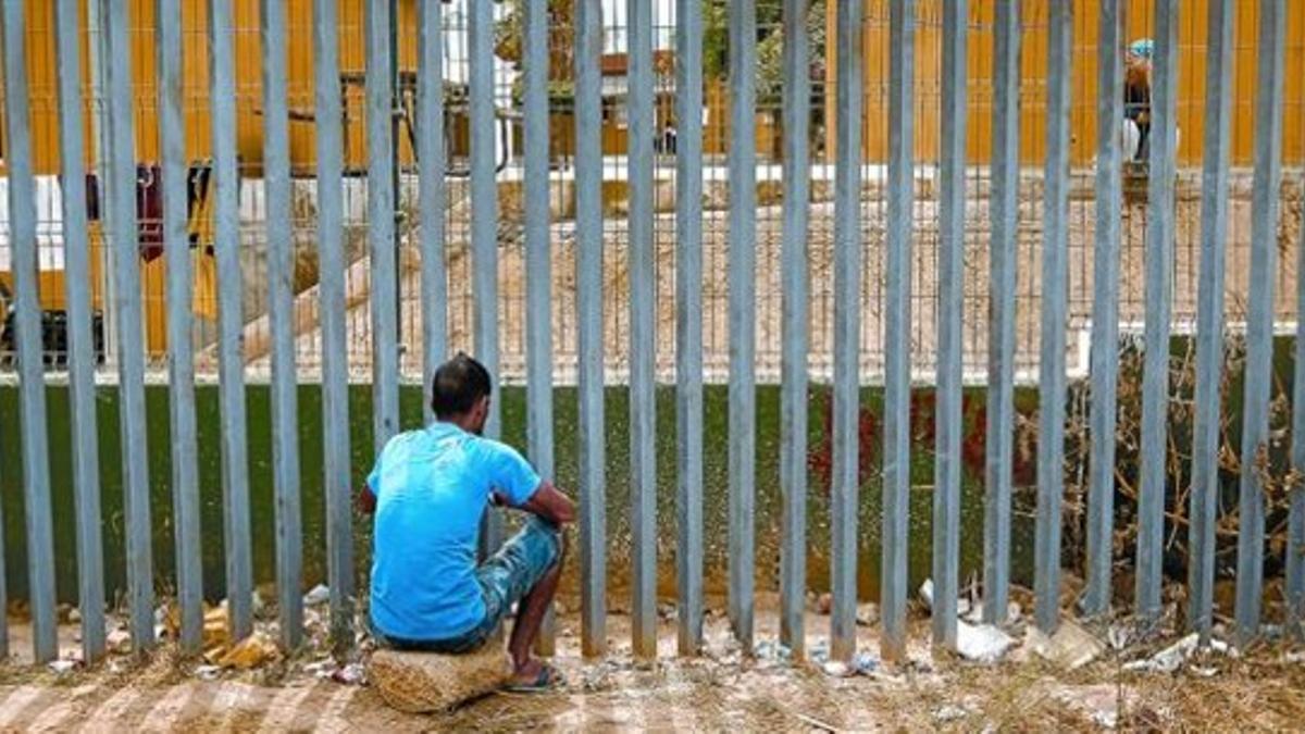 Un inmigrante sentado frente a la valla del CETI de Melilla habla con una mujer que se halla en el interior del centro, el jueves pasado.