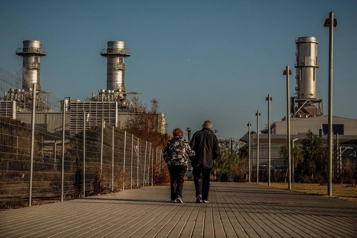 Dos personas paseando en el barrio de La Catalana, en Sant Adrià de Besòs, con las centrales de ciclo combinado de Endesa y Naturgy al fondo.