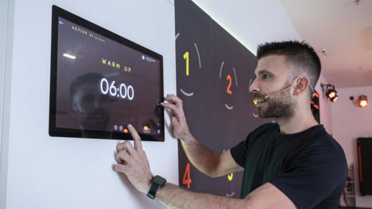 Por la izquierda,  una usuaria salta  sobre un cajón,  un monitor muestra una de las pantallas led, calentamiento previo al inicio de la sesión y, a la derecha, una usuaria salta  durante una sesión.  |  VALENTINA CIUCA