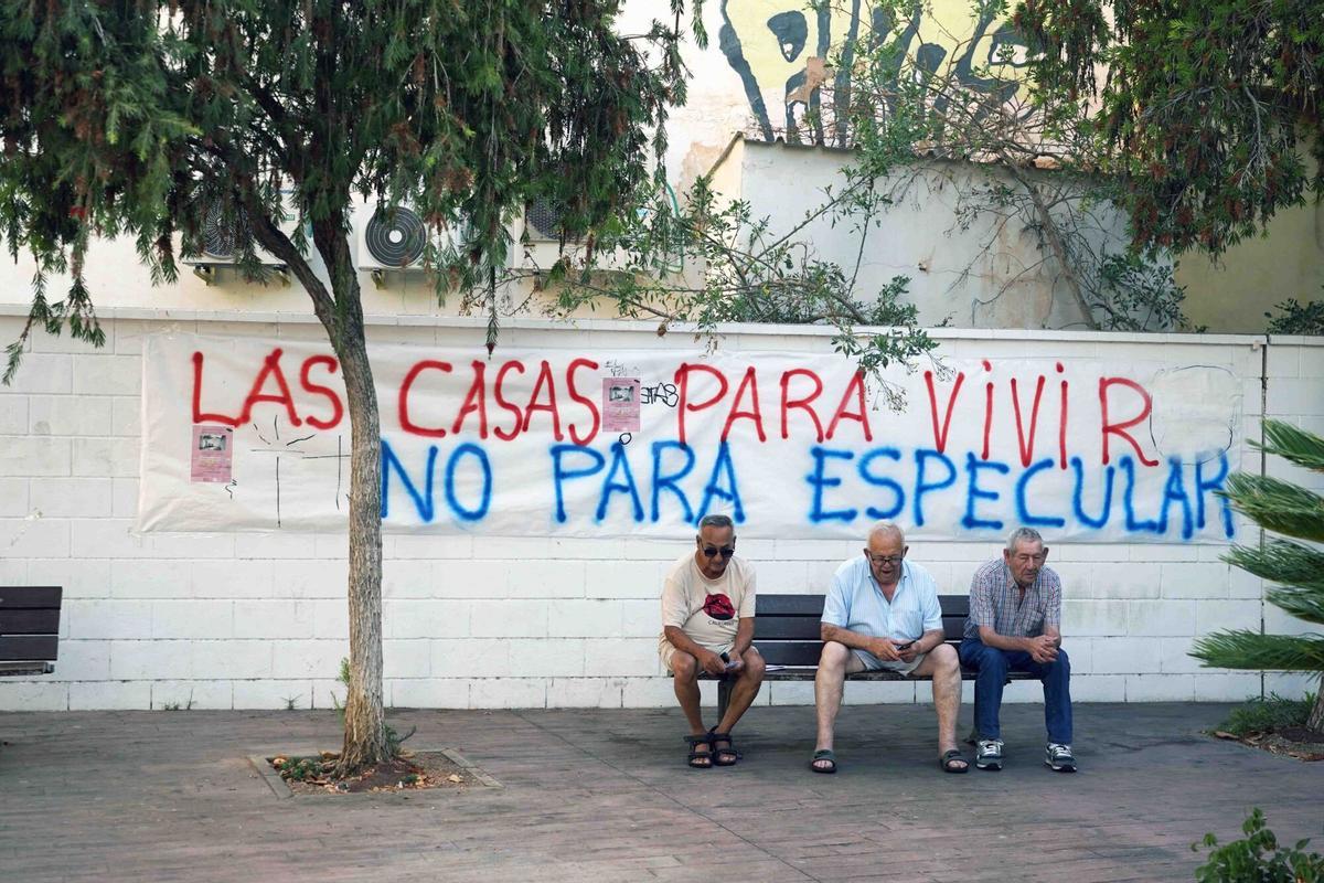 Vecinos, sentados delante de un cartel que reivindica la vivienda digna en la barriada de El Palo
