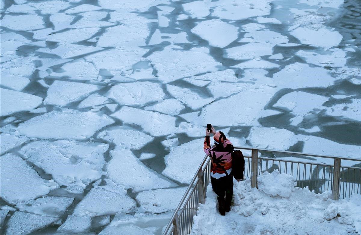 Un peatón se detiene para tomar una fotografía del hielo sobre el río Chicago.