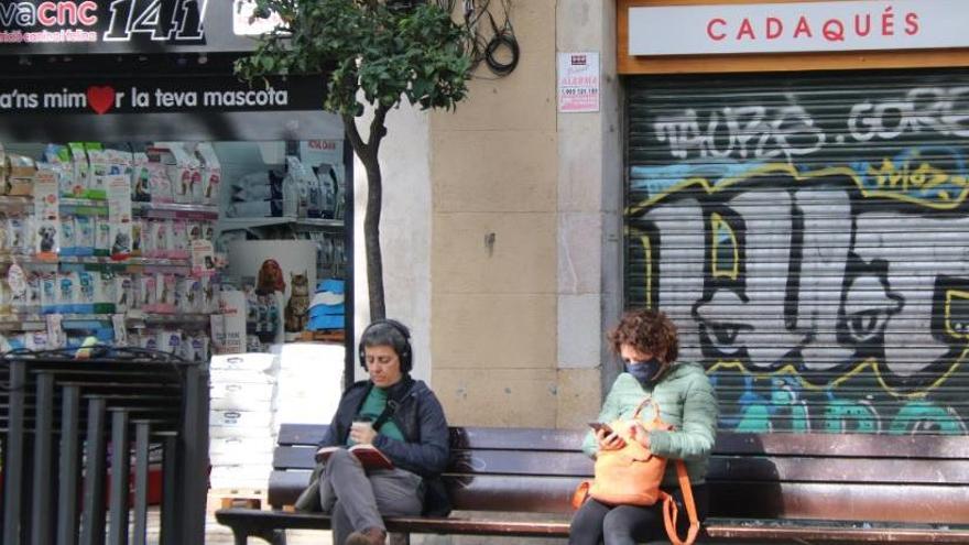Dues dones assegudes a la plaça de la Vila de Gràcia, davant un restaurant tancat |