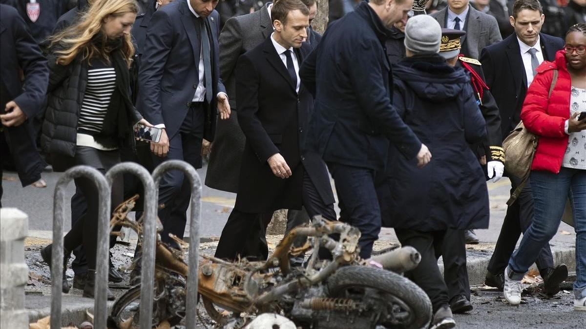 Emmanuel Macron pasa cerca de una motocicleta incendiada en los disturbios de ayer.