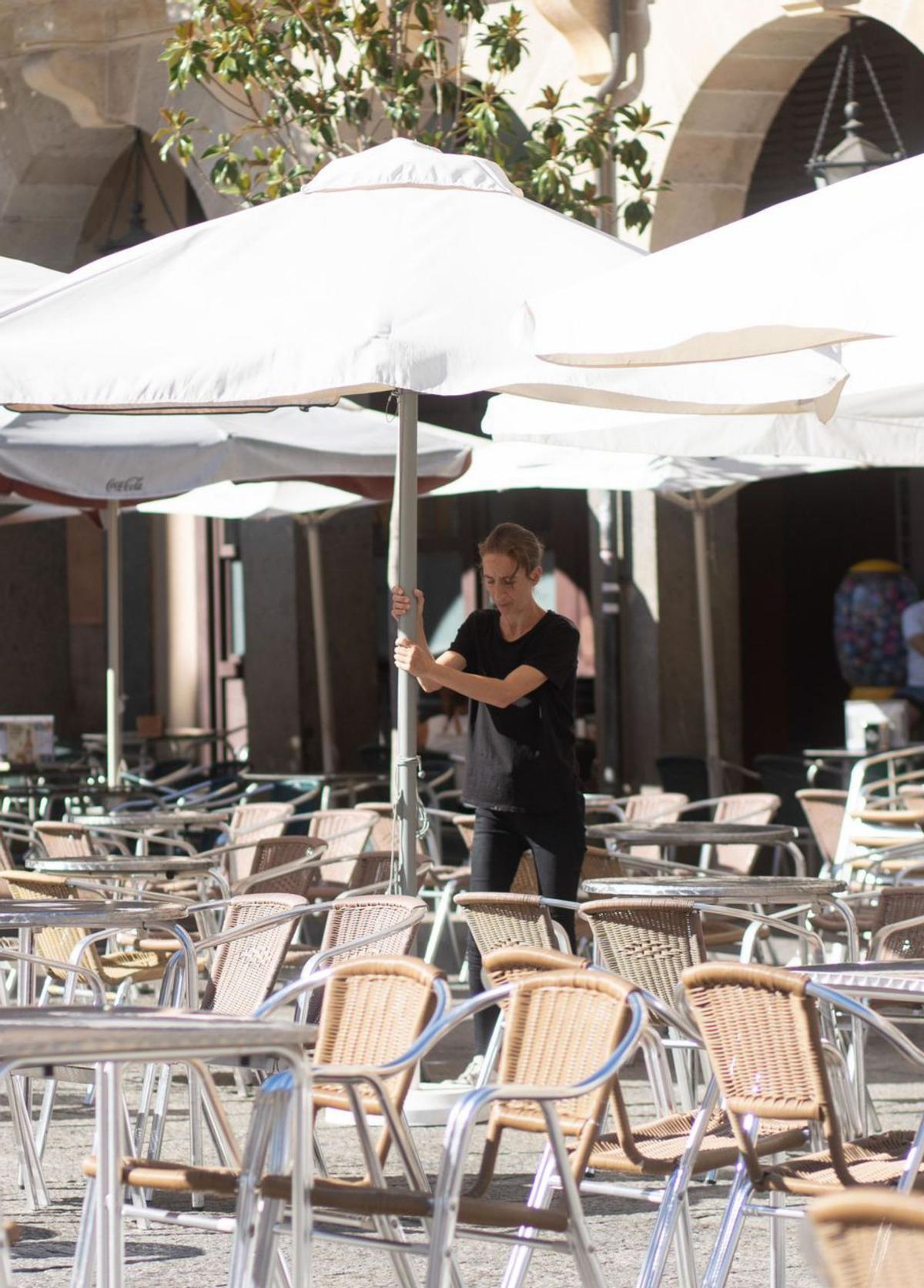 Una camarera coloca sombrillas en la terraza de un bar. | Emilio Fraile