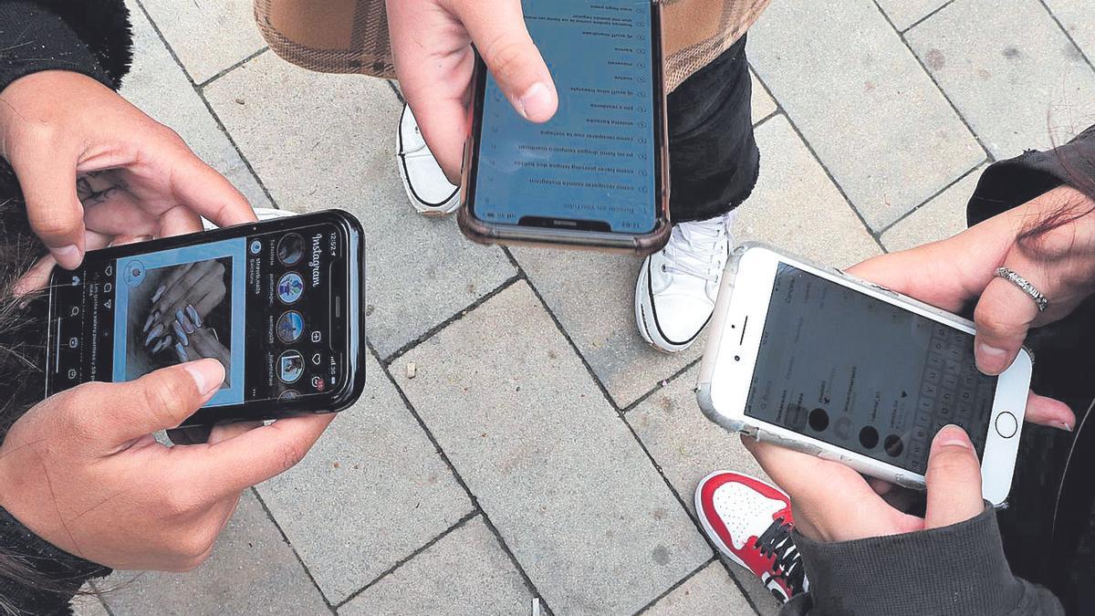 Jóvenes consultan sus redes sociales desde sus teléfonos móviles