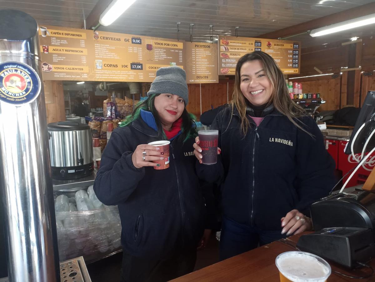 Dos camareras de la caseta de hostelería del mercado navideño de la Plaza de España de Madrid sirven dos vasos de vino caliente, una de las bebidas estrella.