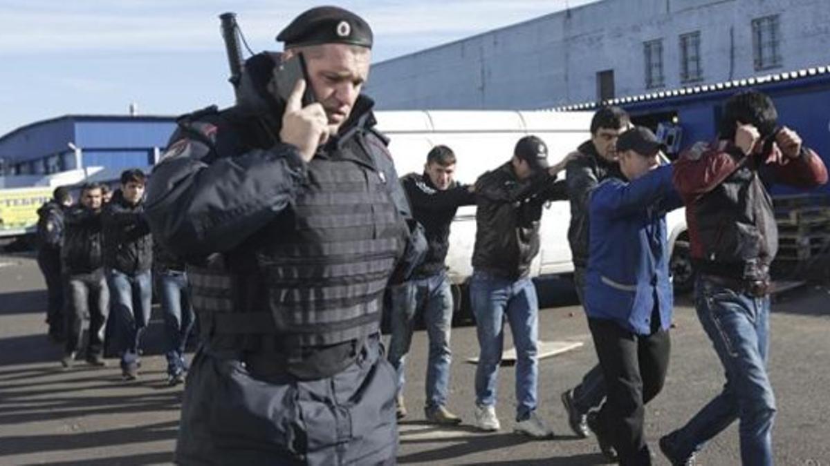 Un agente de policía habla por teléfono mientras vigila a un grupo de inmigrantes detenidos, el día 14 en Moscú.