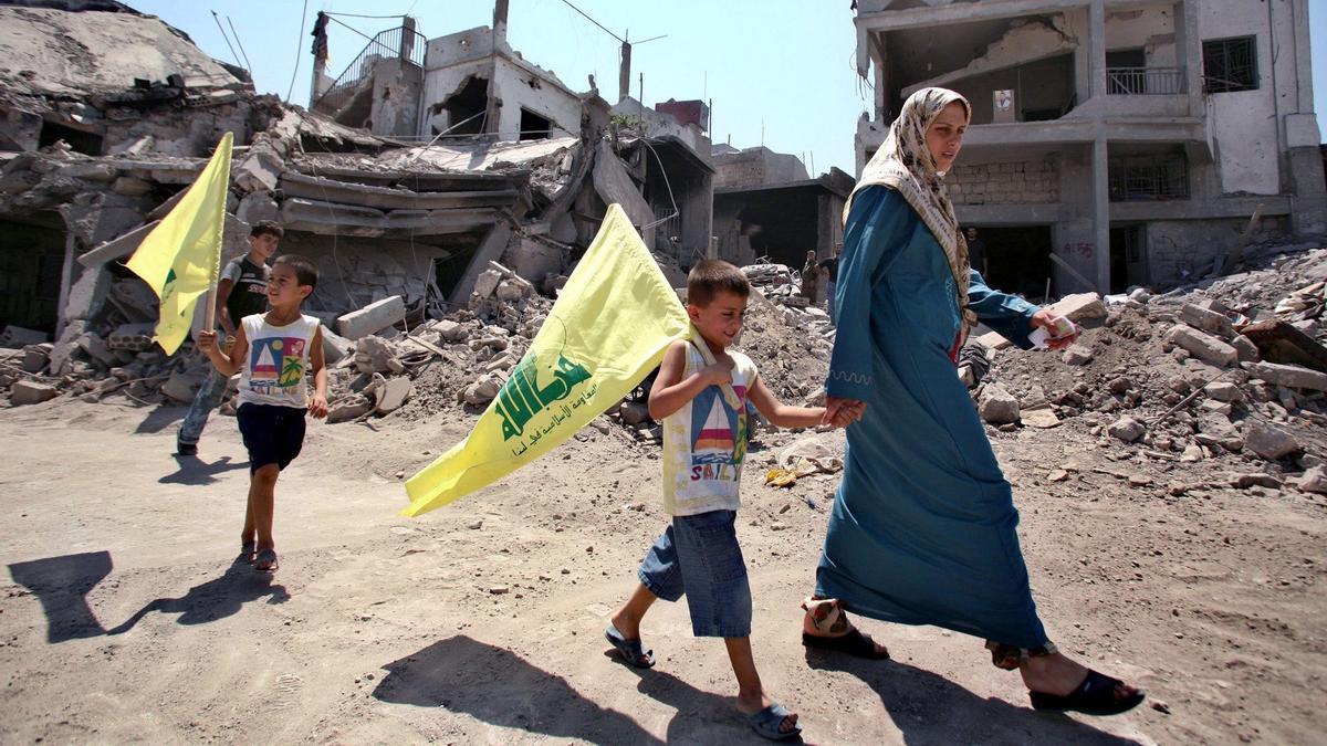 A Lebanese woman and her children, holding Hizbollah flags, walk past the rubble of houses damaged during the recent conflict between Israel and Lebanon’s Hizbollah in Saddikine village, south Lebanon, August 22, 2006. REUTERS/Ammar Awad (LEBANON)