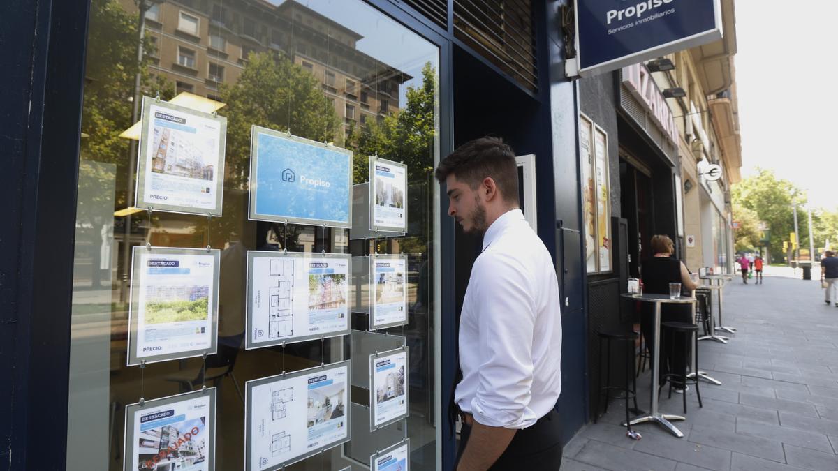 Un joven observa varias ofertas de vivienda de segunda mano en una inmobiliaria de Zaragoza.