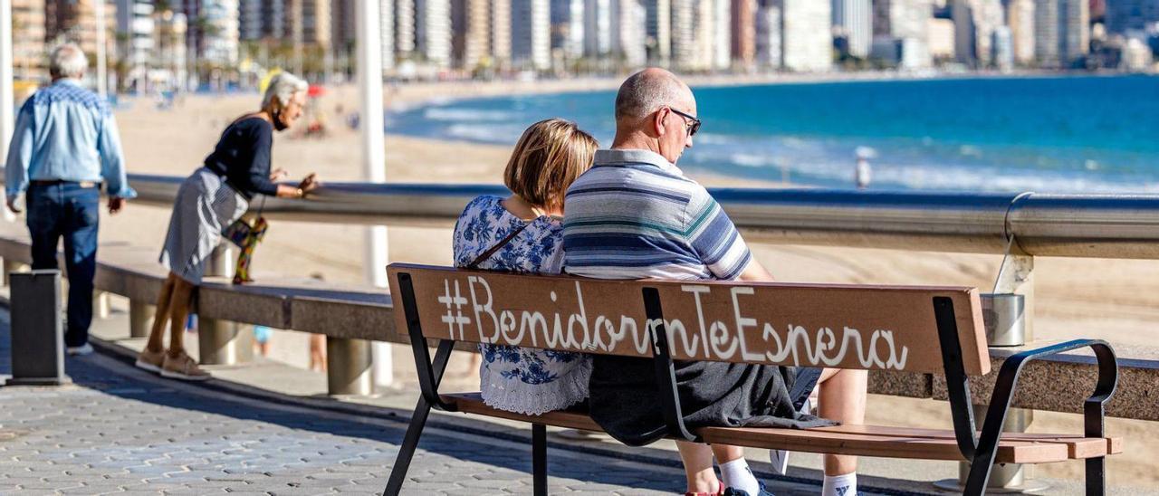 Turistas disfrutan de un día soleado en Benidorm mientras observan el mar y pasean junto a la playa.  |