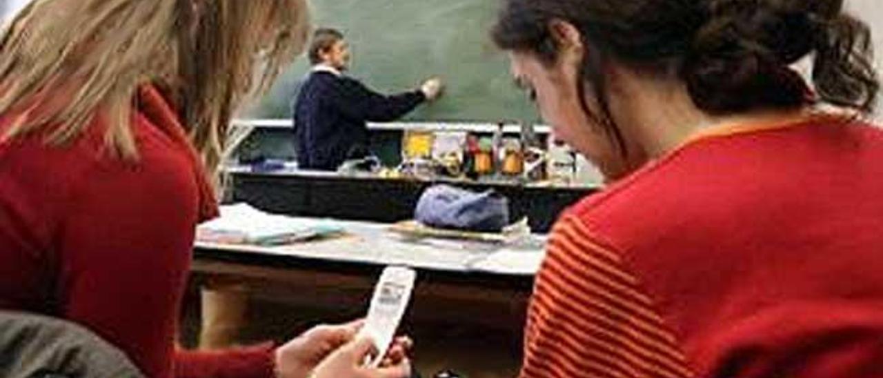 Dos alumnas consultan sus teléfonos móviles en clase.